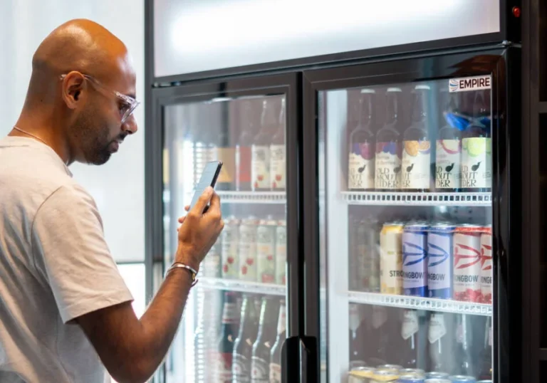Man scanning Strongbow cider packaging with a smartphone in a refrigerated store display using NaviLens accessibility technology